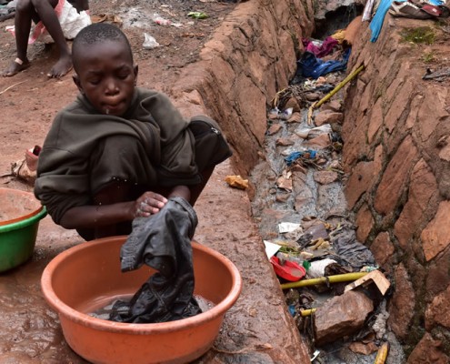 Street boy washing his clothes next to open sewer
